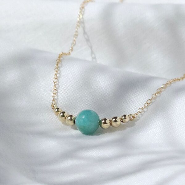 Gold necklace with turquoise bead on fabric.