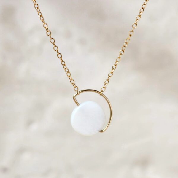 Gold necklace with round white pendant.