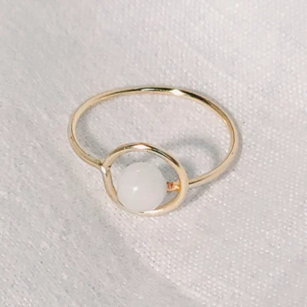 Gold ring with white gemstone on fabric.
