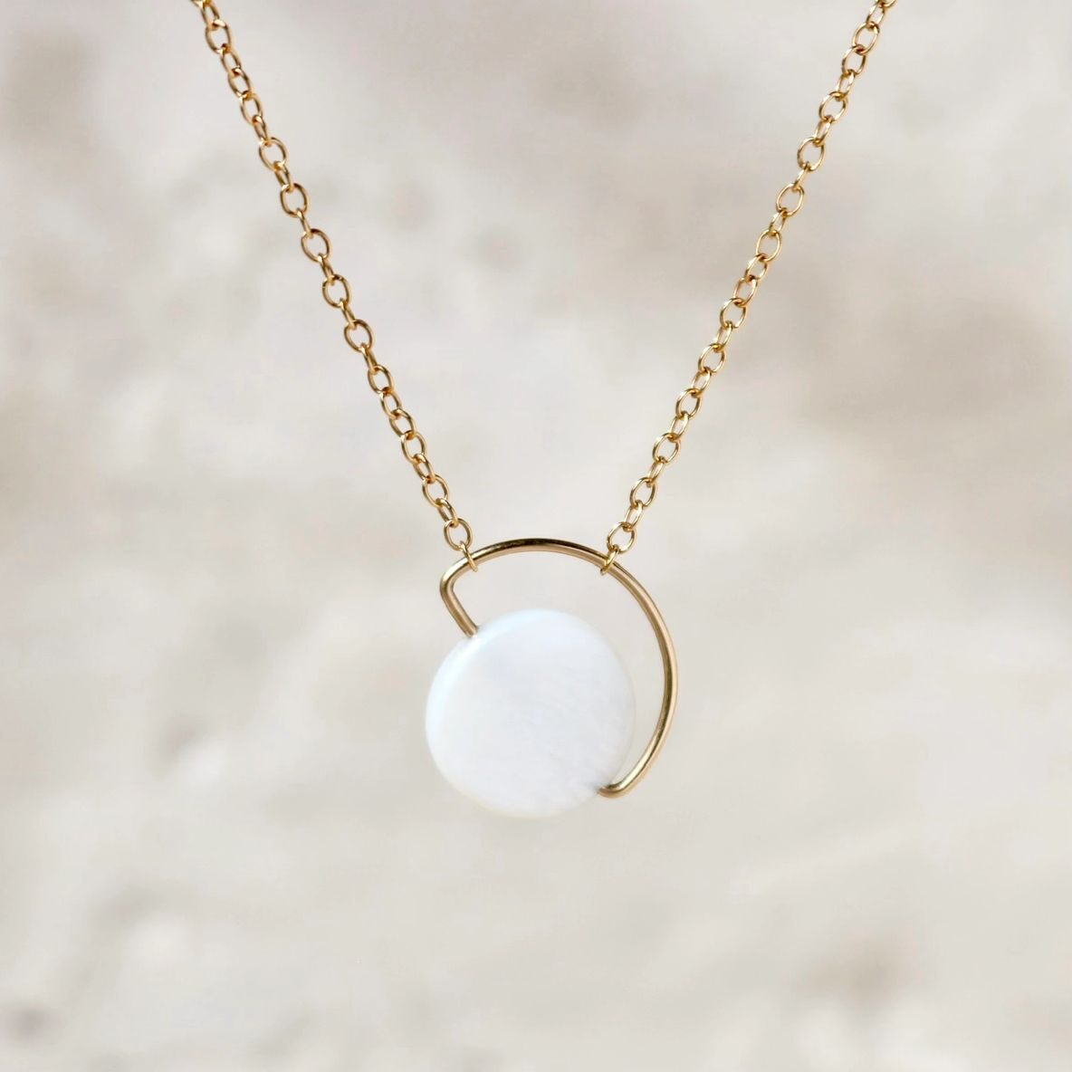 Gold necklace with round white pendant.